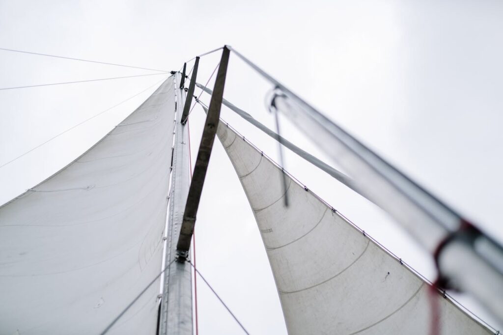 Close-up low angle shot of a sailboat's sails against a cloudy sky, highlighting the mast and rigging.