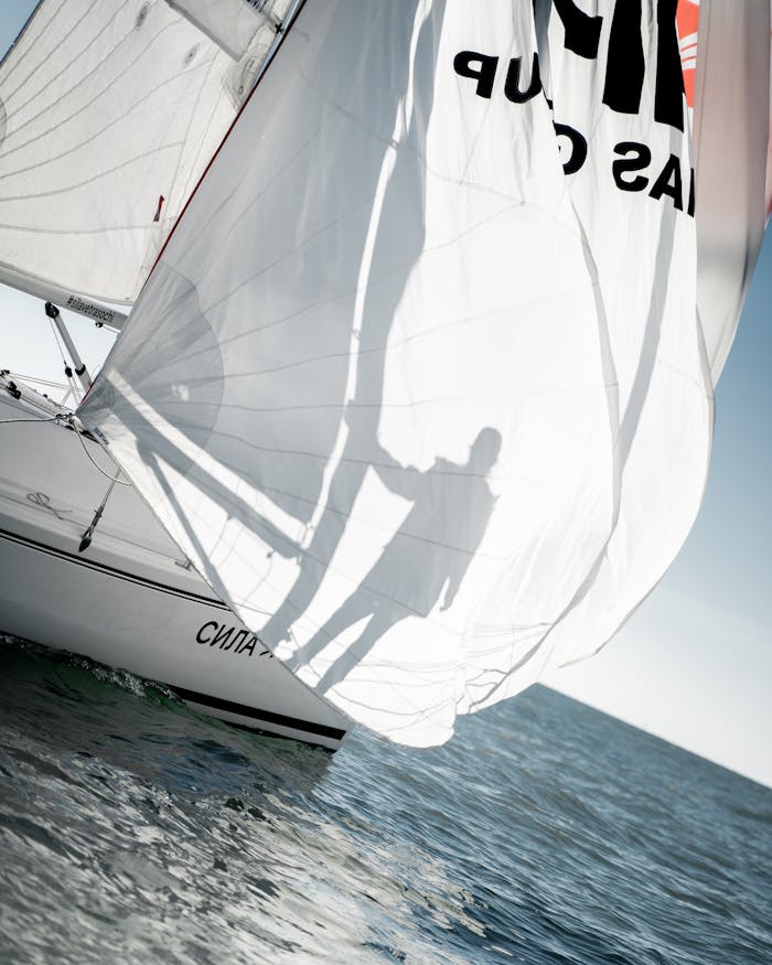 Dynamic shot of a sailing boat with shadows casting on the sail over open sea.